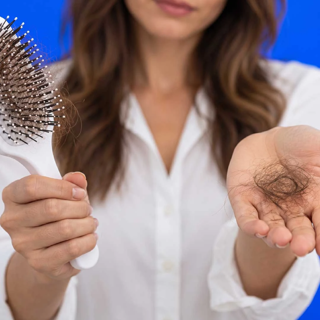 A woman holding a hairbrush in one hand and a clump of shed hair in the other palm
