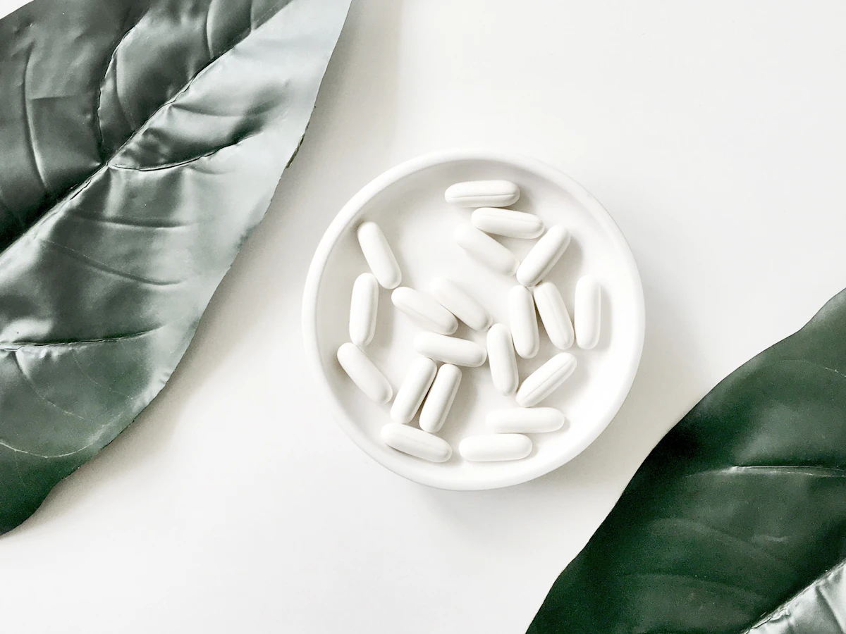 White capsules in a round dish between two green leaves