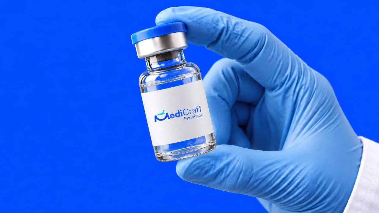 A gloved hand holding a MediCraft vial up against a blue ground